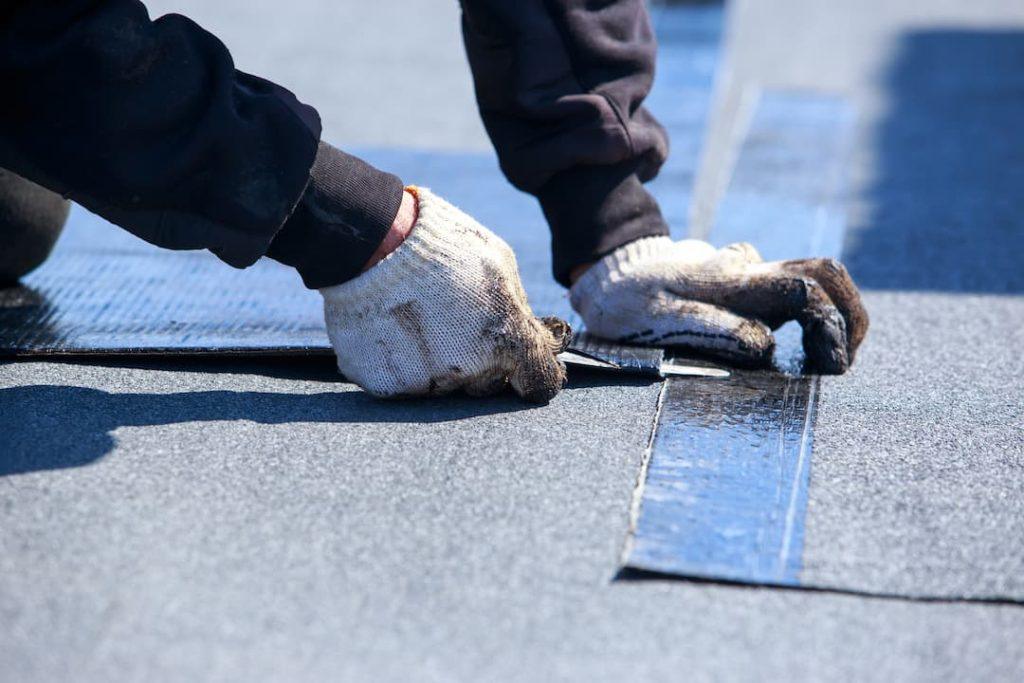 Flat roofing being laid by person wearing black hoodie and white gloves